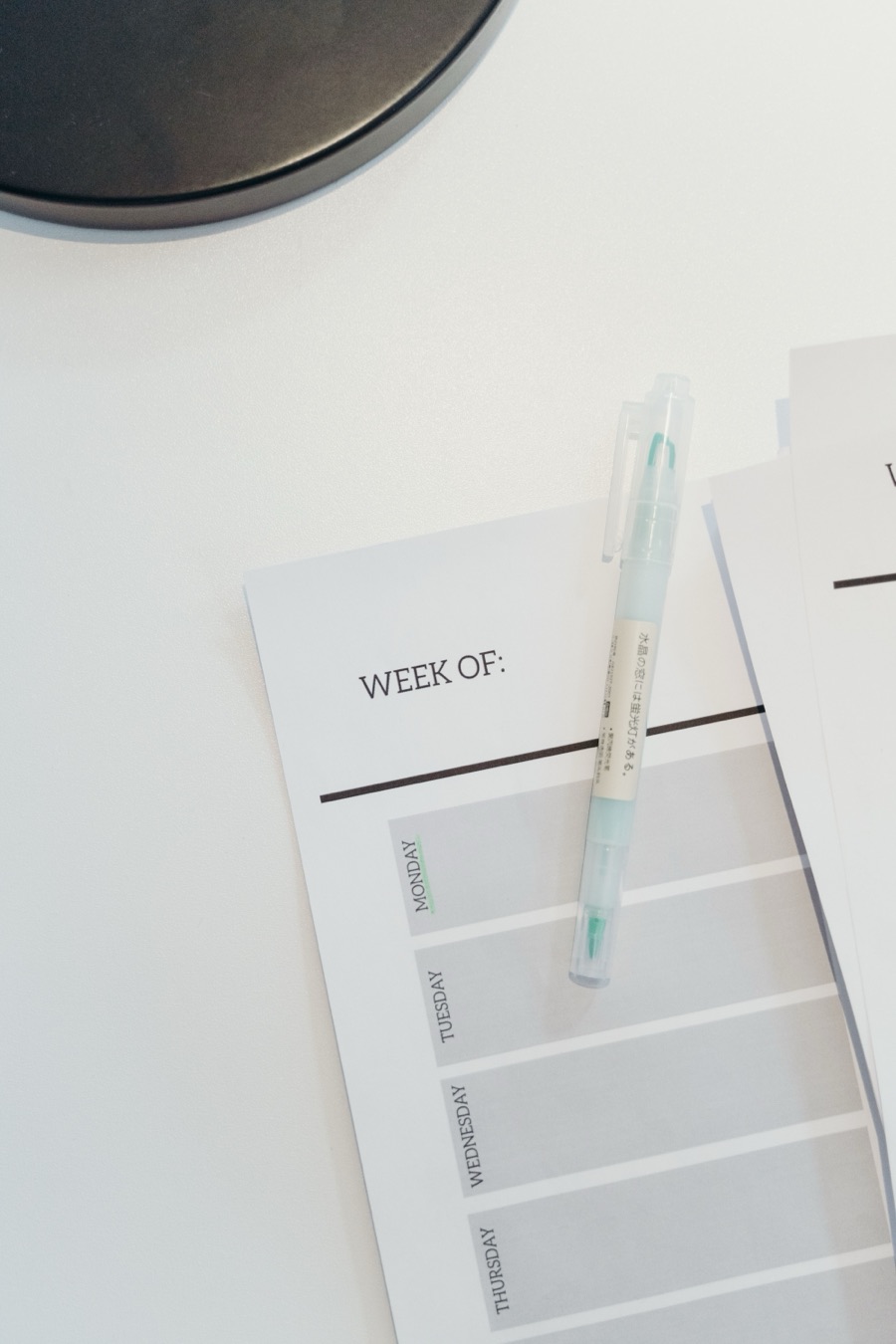 A blank weekly planner and a highlighter pen on a white desk
